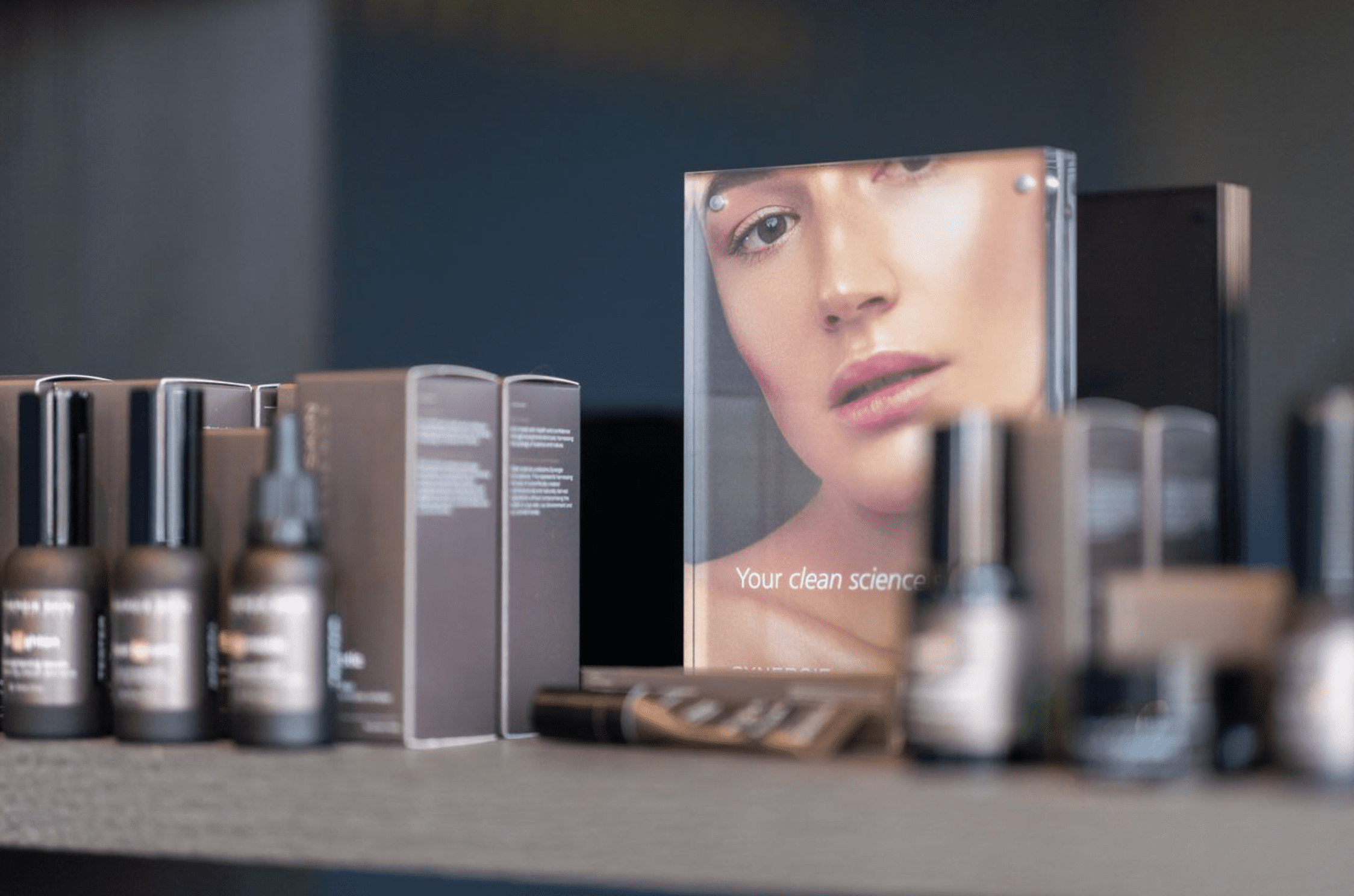 A display of various skincare products with a prominent advertisement featuring a close-up portrait of a woman's face and the caption "your clean science" in a modern, sleek setting.
