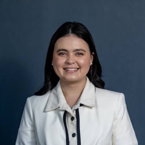 A woman with shoulder-length dark hair smiling at the camera, wearing a white collar jacket over a black blouse against a products-themed dark blue background.