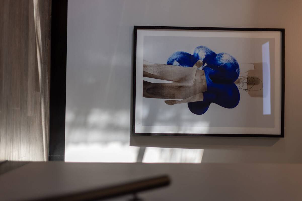 A framed photograph on a wall showing a close-up image of hands wearing blue boxing gloves, partially obscured by the glare on the glass. the room is dimly lit, emphasizing the artwork.