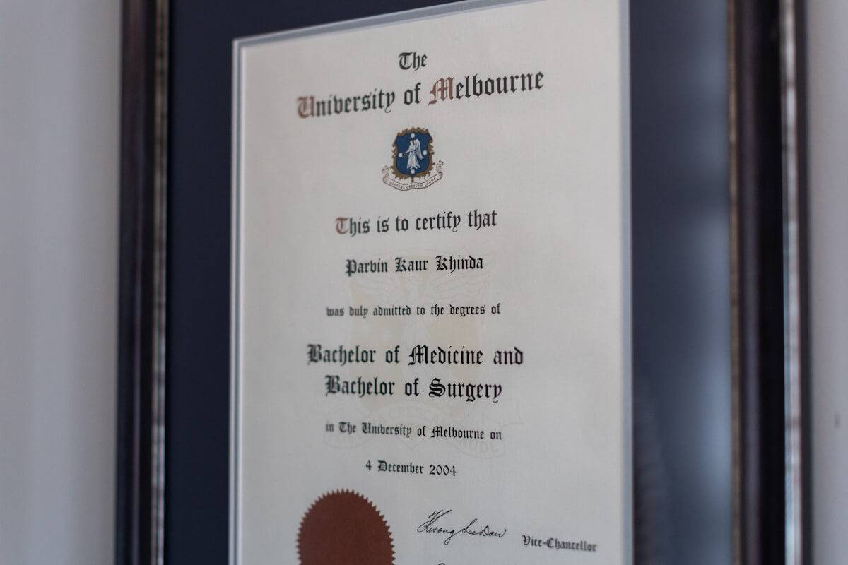 A framed degree certificate from the university of melbourne for a bachelor of medicine and surgery, dated december 4, 2004, displayed on a wall.