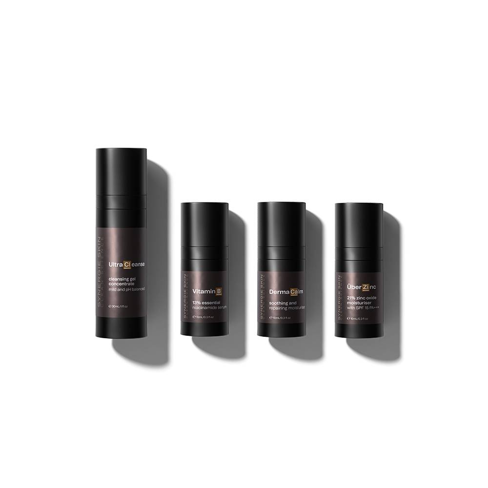 Four cylindrical Synergie skincare bottles with labels including "Anti-Redness Kit," "vitamin b3," "derma calm," and "clear zinc" arranged in a row.