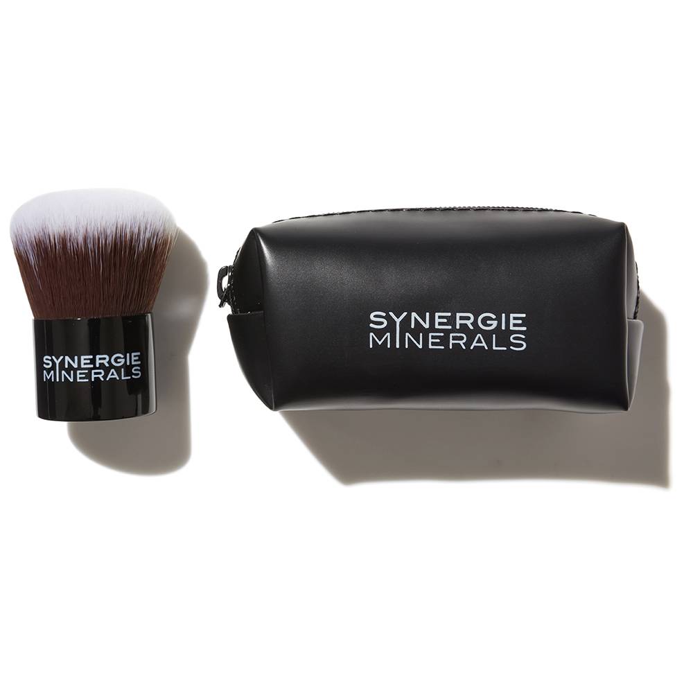 A black cosmetic pouch labeled "synergie minerals" alongside a matching makeup brush with a dense, flat top, all against a white background.