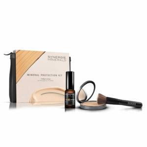 A synergie minerals makeup kit including a compact powder, a liquid bottle, a kabuki brush, and packaging with a wooden design and brand logo.