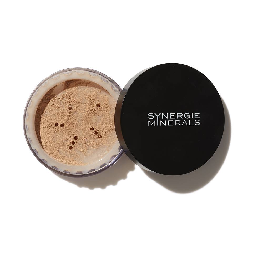 A container of synergie minerals loose powder makeup with its lid off, showing the light beige powder inside. the lid, placed next to the container, displays the brand logo.