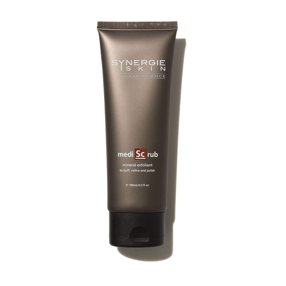 A tube of synergie skin medisc rub mineral exfoliant stands upright on a plain white background, displaying its sleek, brown packaging with product details.