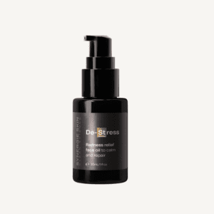 Black bottle of "de-stress redness relief face oil" with a pump dispenser, labeled for calming and repairing skin, isolated on a white background. the container holds 30 ml/1oz of the product.