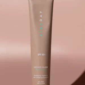 A tube of Golden Glow SPF50+ Dreamscreen 75ml stands upright on a matching beige background, casting a right-side shadow. The packaging displays product details in white and mint green text.