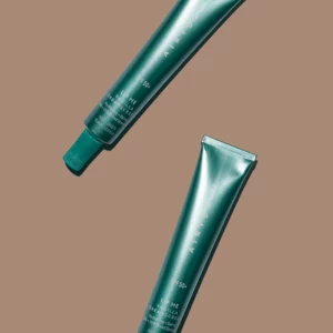 Two identical green metallic tubes labeled "Lip Me Vanilla SPF50+ Dreamscreen 15ml" with screw caps are arranged diagonally on a plain brown background.