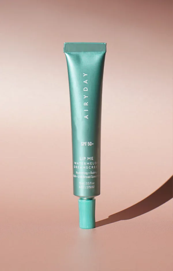 A teal tube of Lip Me Watermelon SPF50+ Dreamscreen 15ml stands upright on a pink surface with its screw cap secured, casting a distinct shadow to one side.