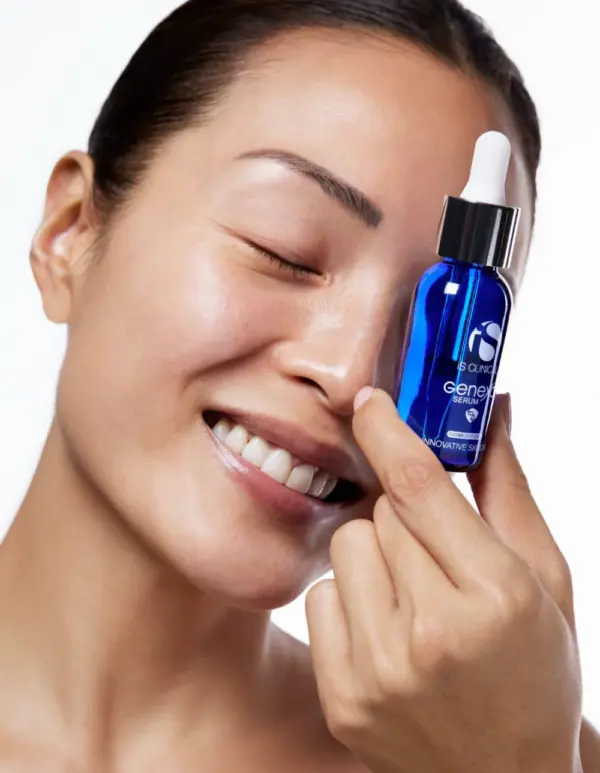 A smiling person with closed eyes holds a blue dropper bottle of GeneXC Serum 15ml next to their face, displaying clear and smooth skin.