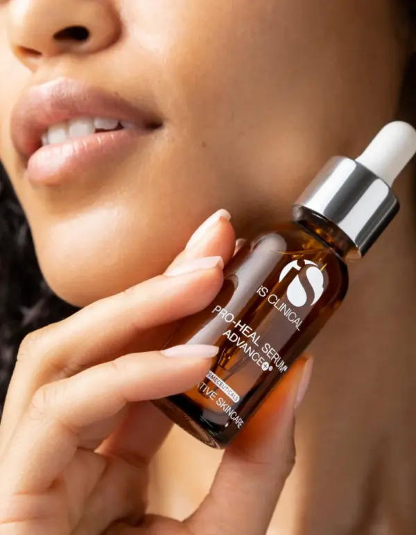 A person holds a 30ml brown glass dropper bottle labeled "Pro-Heal Serum Advance+ 30ml" close to their face, showing part of their lips and chin.